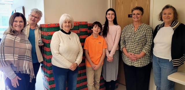 Volunteers pose next to stacked boxes of donations for a charitable initiative, showcasing community support and engagement.