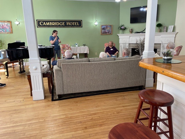 Residents interact in a cozy lounge at Cambridge Hotel, featuring a piano, comfortable seating, and a warm, inviting atmosphere.